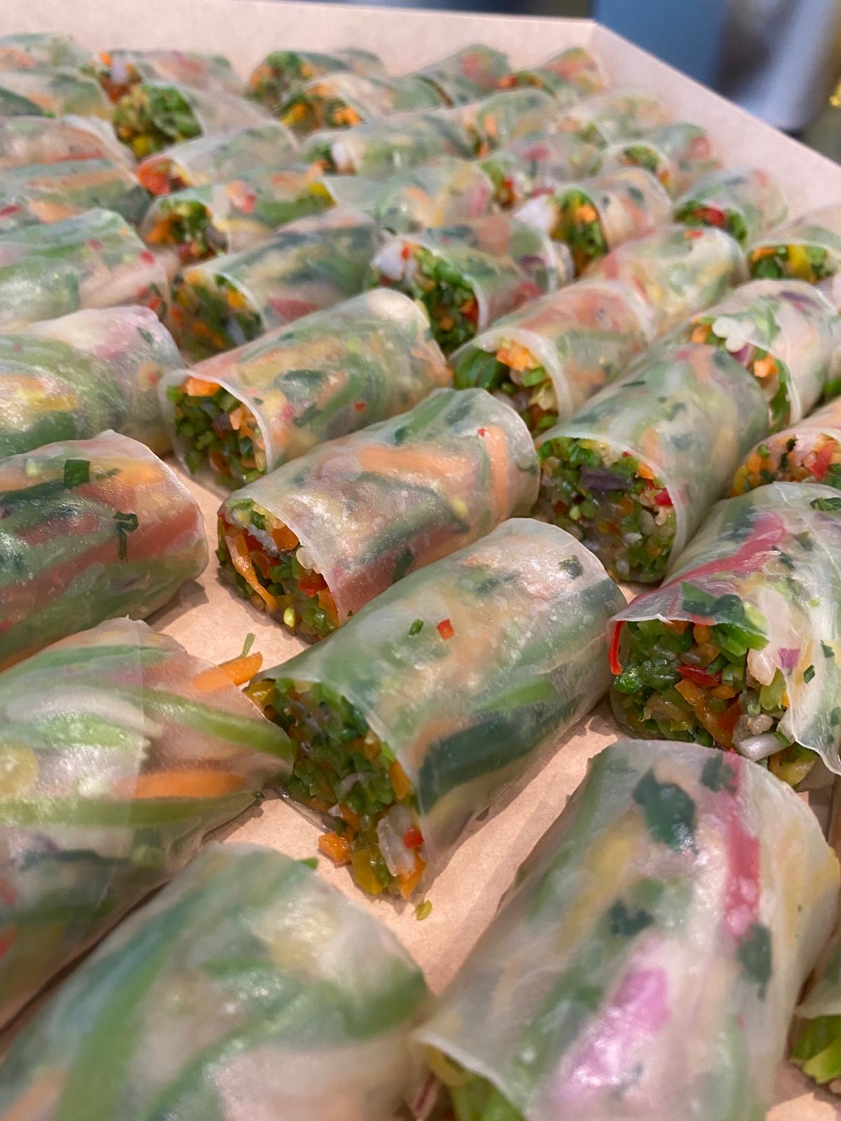 A close-up of neatly arranged fresh vegetable spring rolls wrapped in translucent rice paper, showcasing vibrant colors and textures from a variety of vegetables.