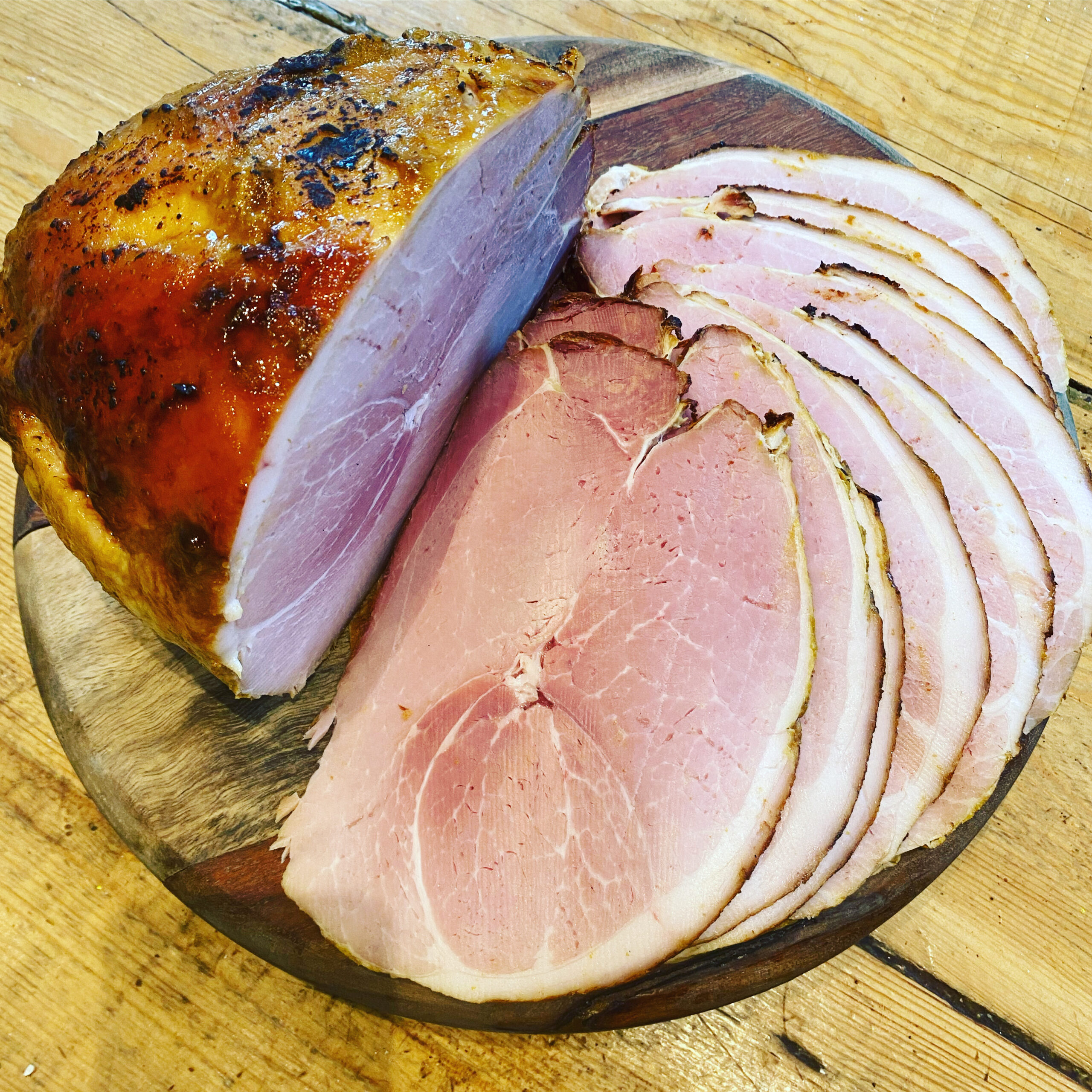 A beautifully roasted ham with glossy skin beside neatly sliced pink ham on a wooden serving board.