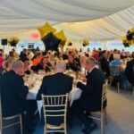 Attendees enjoying a formal dinner with gold and black star-shaped balloons in a beautifully decorated marquee.