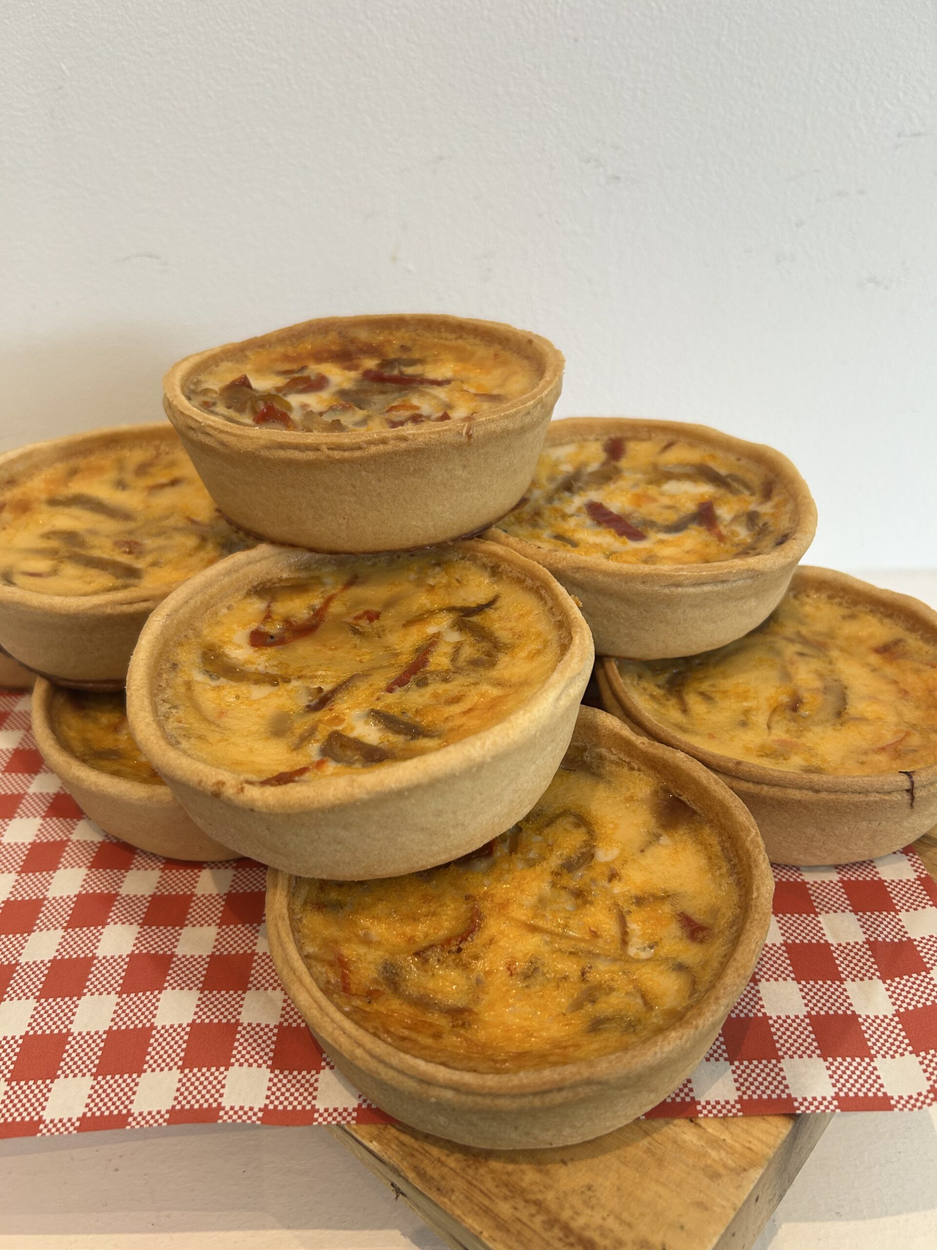 Stack of mini quiche bowls on a checkered napkin, showcasing a golden, cheesy filling.