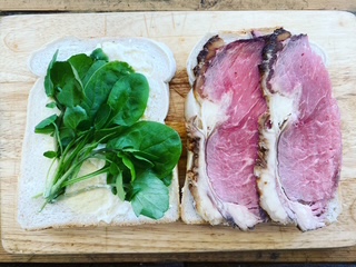 Sliced roast beef and fresh greens on bread, ready for assembly.