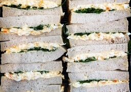 A close-up view of neatly arranged layered sandwiches with fillings of green leafy vegetables and egg salad.