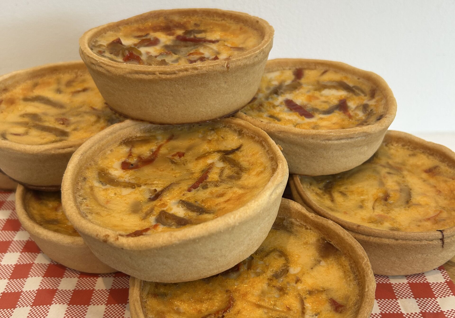 Stack of mini quiche bowls on a checkered napkin, showcasing a golden, cheesy filling.
