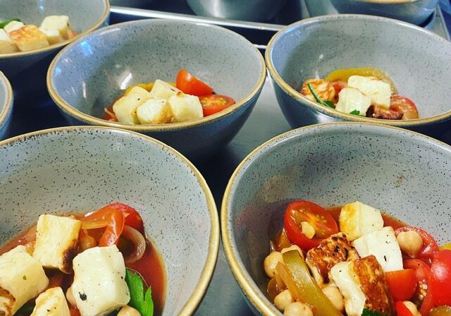 A close-up view of multiple bowls filled with a vibrant vegetable and cheese soup, featuring colorful ingredients like tomatoes, herbs, and chunks of cheese.