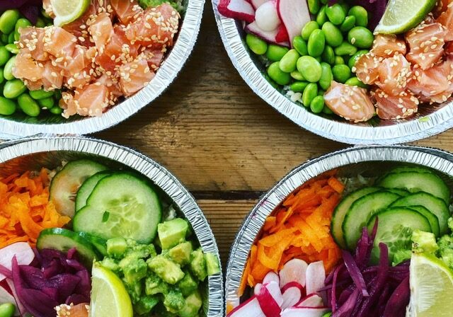Four visually appealing salmon poke bowls with fresh vegetables, avocado, and lime, arranged on a wooden table.