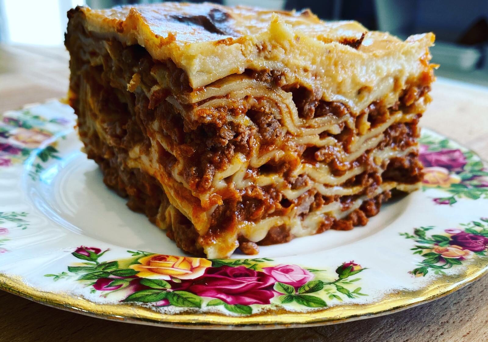 A slice of homemade lasagna layered with meat and cheese on a floral plate.